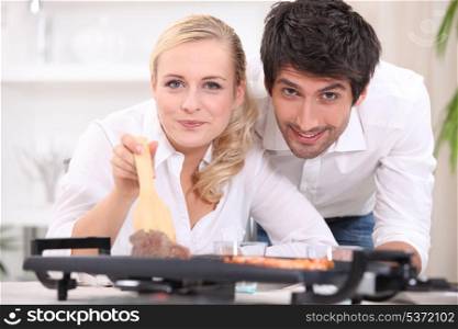 Couple cooking steak and prawns on a table top hotplate