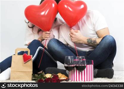 couple covering faces with red heart balloons