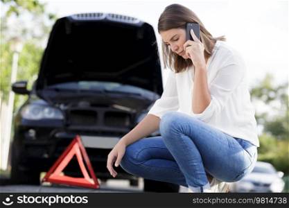 couple crouching by broken down car using her smartphone