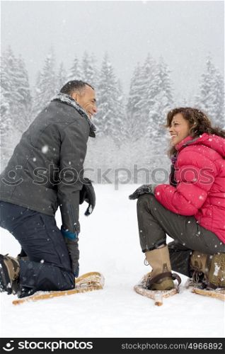 Couple crouching in the snow wearing snowshoes