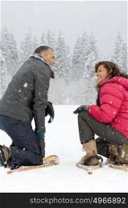 Couple crouching in the snow wearing snowshoes