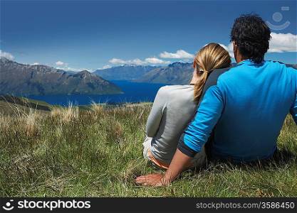 Couple cuddling looking over lake and hills back view