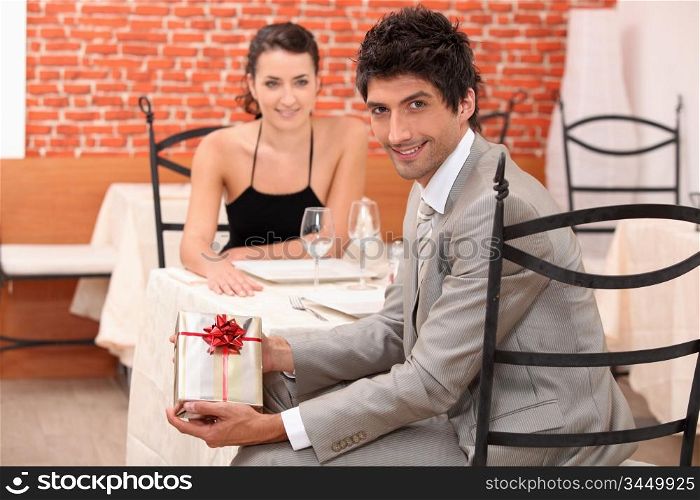 couple dining in a romantic restaurant, the man is showing a present