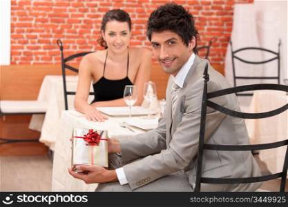 couple dining in a romantic restaurant, the man is showing a present