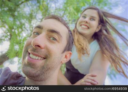 Couple doing silly and funny faces while taking selfie picture in the park.