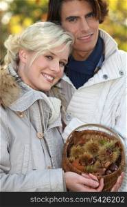 couple dressed in warm clothes, woman is holding a wickerwork basket full of chestnuts