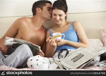 Couple Eating Breakfast And Reading Newspaper In Bed