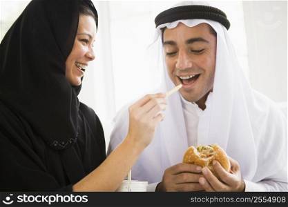 Couple eating fast food in living room and smiling (high key/selective focus)