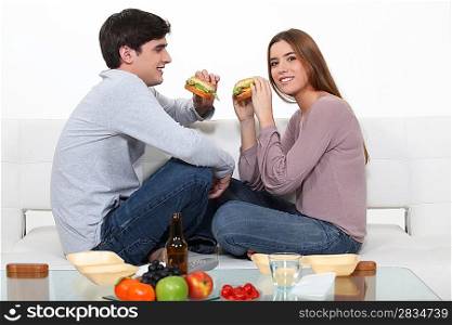 couple eating hamburgers on the couch