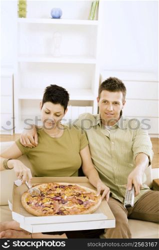 Couple eating pizza and watching TV at home.