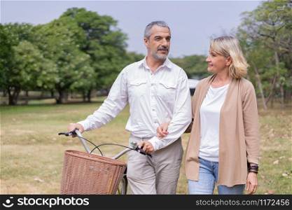 Couple elderly relaxing at park walking with bike and talking together in morning. The concept of good health and relax