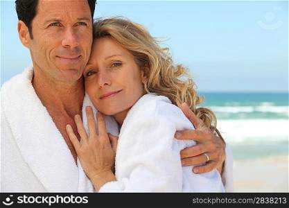 Couple embracing by the sea in toweling robes