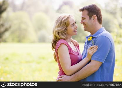 Couple embracing outdoors holding flower smiling