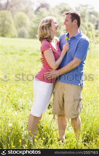Couple embracing outdoors holding flower smiling
