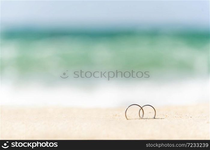 Couple engagement wedding rings on summer tropical sand beach with copy space. Display design for honeymoon travel agency concept. Wedding rings on sand with holiday vacation for couple propose marry