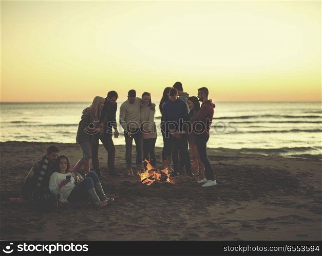 Couple enjoying bonfire with friends on beach. Couple using cell phone during beach party with friends drinking beer and having fun colored filter