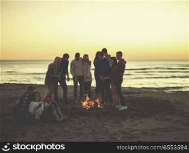Couple enjoying bonfire with friends on beach. Couple using cell phone during beach party with friends drinking beer and having fun colored filter