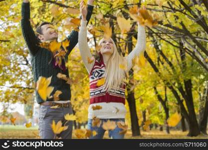 Couple enjoying falling autumn leaves in park