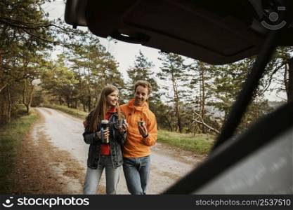 couple enjoying hot beverage while road trip with car