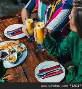 Couple enjoying romantic vegetarian dinner, drinking fresh orange juice on a date. Couple sitting at wooden table, wearing colorful outfit.   