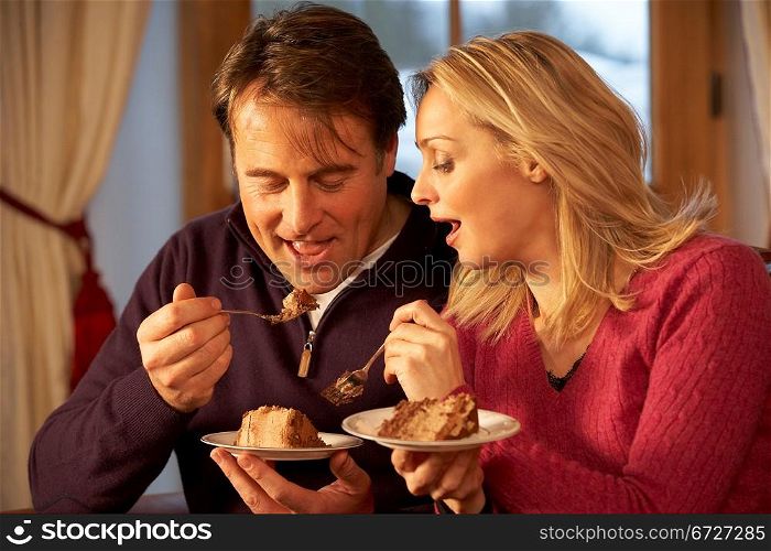 Couple Enjoying Slice Of Cake Sitting On Sofa
