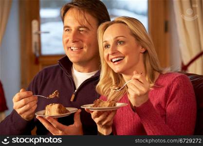 Couple Enjoying Slice Of Cake Sitting On Sofa Watching TV