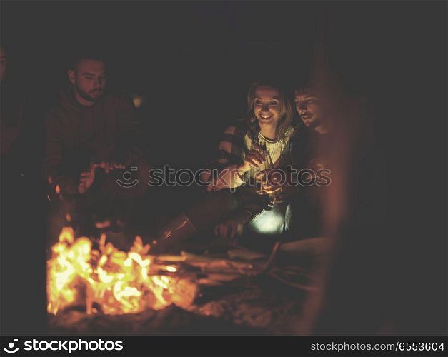 Couple enjoying with friends at night on the beach. Young Couple Sitting with friends Around Campfire on The Beach At Night drinking beer colored filter