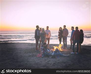 Couple enjoying with friends at sunset on the beach. Young Couple Sitting with friends Around Campfire on The Beach At sunset drinking beer colored filter