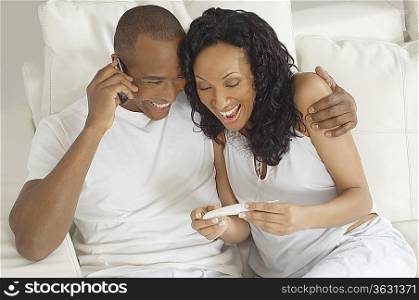 Couple examining pregnancy test in bed, man using mobile phone