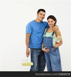 Couple expecting baby holding paintbrushes and smiling.
