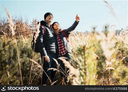 Couple exploring nature while vacation trip. Hikers with backpacks on way to mountains. People walking through tall grass along path in meadow on sunny day. Active leisure time close to nature