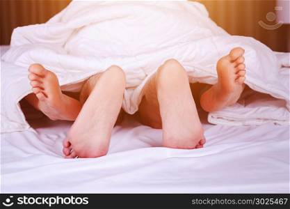 couple feet seen from under blanket on a bed