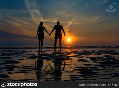Couple hand in hand towards the sea in a dawn late summer in silhouettes