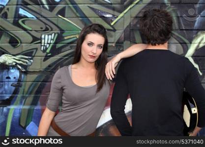 Couple hanging out by a wall painted with graffiti