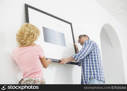 Couple hanging picture frame on wall in new house