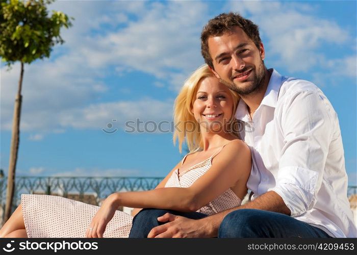 Couple having a city break in summer sitting on a brick wall in the sunlight