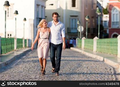 Couple having a city break in summer walking on a bridge over a river in the evening light