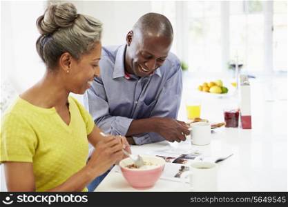 Couple Having Breakfast And Reading Magazine In Kitchen
