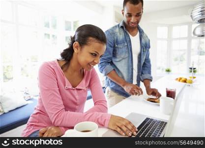 Couple Having Breakfast And Using Laptop In Kitchen