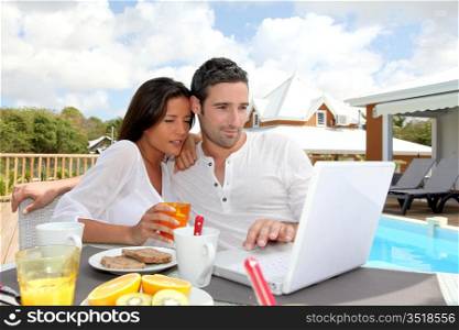 Couple having breakfast outside in front of laptop