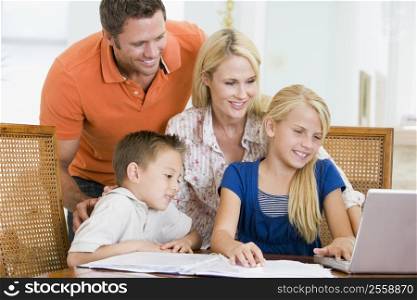 Couple helping two young children with laptop do homework in dining room