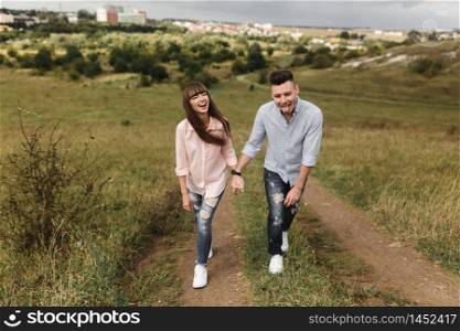 Couple holding hands are walking away. Portrait of a romantic young man and woman in love in nature. husband and wife pass through the field and holding hands climbing the mountain. Couple holding hands are walking away. Portrait of a romantic young man and woman in love in nature. the couple climbs up the hill