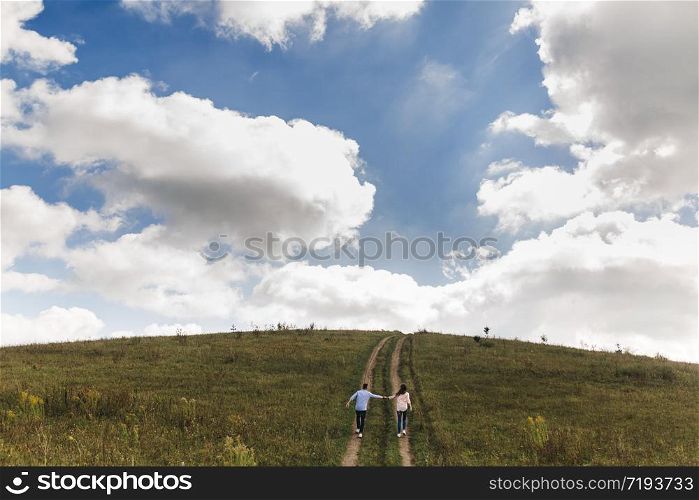 Couple holding hands are walking away. Portrait of a romantic young man and woman in love in nature. husband and wife pass through the field and holding hands climbing the mountain. Couple holding hands are walking away. Portrait of a romantic young man and woman in love in nature. the couple climbs up the hill