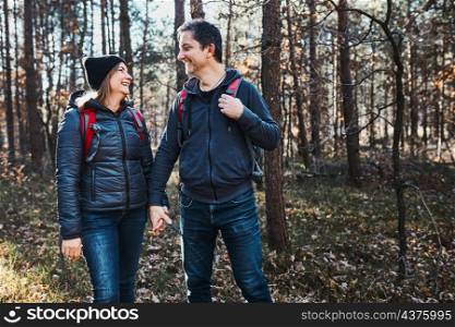Couple holding hands enjoying trip while vacation day. Hikers with backpacks walking on forest path on sunny day. Active leisure time close to nature