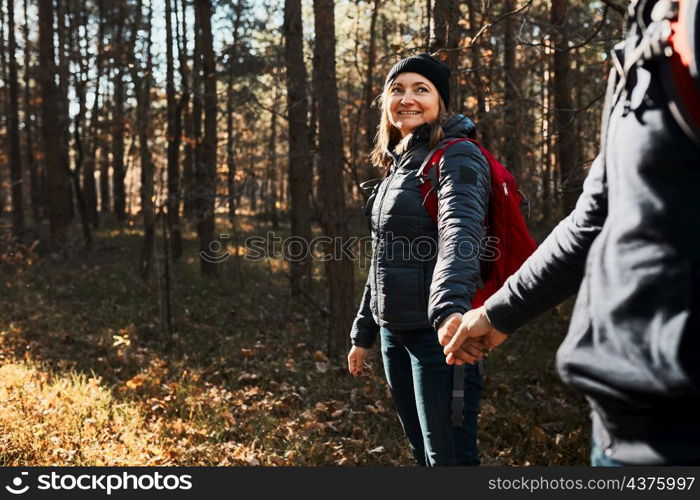 Couple holding hands enjoying trip while vacation day. Hikers with backpacks walking on forest path on sunny day. Active leisure time close to nature