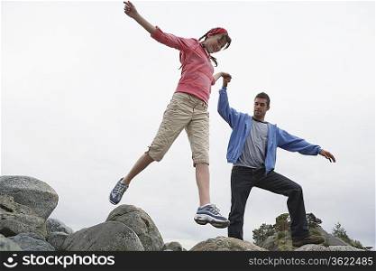 Couple holding hands jumping on rocks