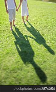Couple holding hands walking on grass low section