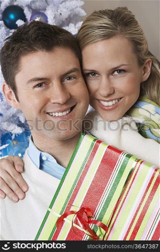 Couple holding present by Christmas tree, portrait