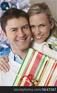 Couple holding present by Christmas tree, portrait