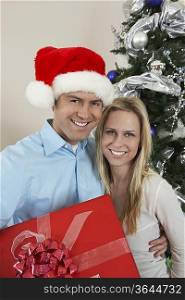Couple holding present in front of Christmas tree